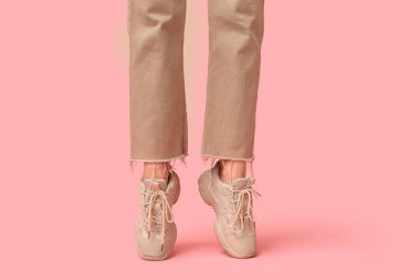 Pembe arka planda bej renkli spor ayakkabılı genç kadın bacakları.