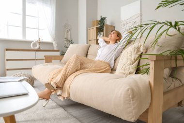 Evdeki bej kanepede dinlenen genç bir kadın.