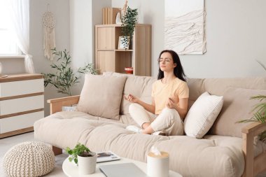 Evdeki bej koltukta oturan genç bir kadın.