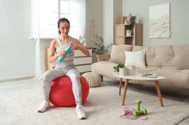 Sportif genç bir kadın evinde spor salonunda su şişesi açıyor.