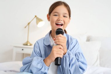 Yatak odasında mikrofonlu küçük kız şarkı söylüyor, yakın plan.