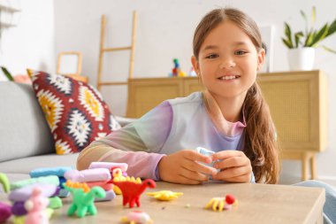 Evdeki masada plastikten heykel yapan küçük bir kız.