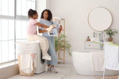 Afro-Amerikalı kadın ve kızı banyoda çamaşır yıkıyorlar.