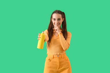 Sprey boyalı genç kadın yeşil arka planda sessizlik hareketi gösteriyor.