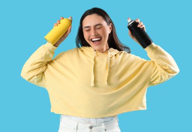 Mavi arka planda sprey boya kutuları olan mutlu genç bir kadın.