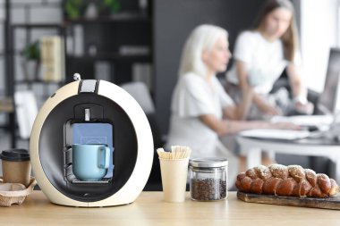 Ofisteki masada modern kahve makinesi ve pasta var.