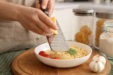 Mutfaktaki masada peyniri lezzetli makarnanın üzerine rendeleyen kadın, yakın plan.