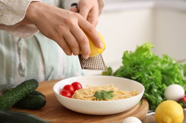 Mutfaktaki makarnanın üzerine limon rendeleyen kadın, yakın plan.