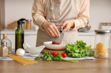Mutfaktaki masada makarna üzerine sarımsak rendeleyen kadın, yakın plan.