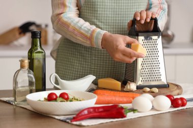 Mutfaktaki masada peynir rendeleyen kadın, yakın plan.