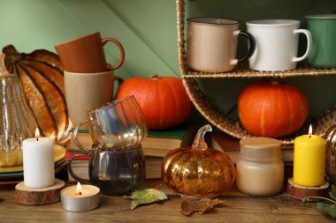 Kabaklı bulaşık takımı, sonbahar yaprakları ve yeşil duvarın yanında yanan mumlar.