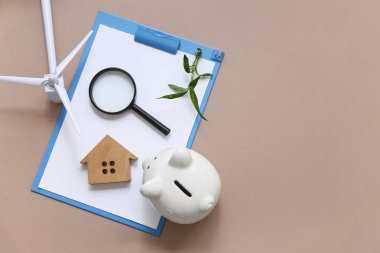 Bitki, büyüteç, ev figürü, kumbarası ve kahverengi arka planda rüzgar türbini olan bir pano. Yeşil Enerji kavramı