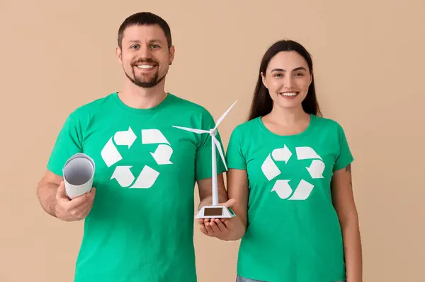 stock image Young couple in t-shirts with recycle signs and wind turbine model on beige background