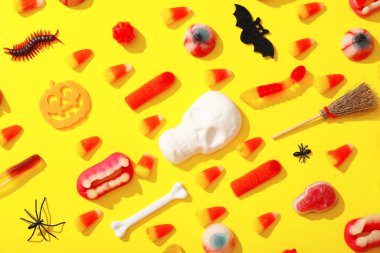 Sarı arka planda Cadılar Bayramı için farklı tatlılar ve dekorasyonlar içeren kompozisyon