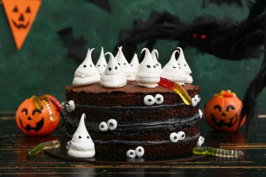 Tatlı Cadılar Bayramı pastası, yeşil arka planda kremalı hayaletler, jöle solucanları, balkabakları ve örümceklerle süslenmiş.