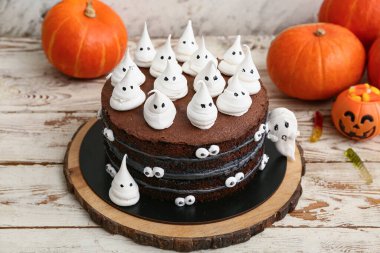 Tatlı Cadılar Bayramı pastası, beyaz ahşap masada hayaletler ve balkabaklarıyla süslenmiş.