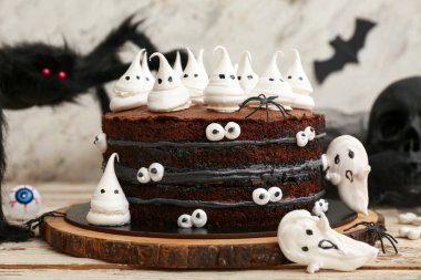 Tatlı Cadılar Bayramı pastası beyaz ahşap masada hayaletler, örümcekler ve gözlerle süslenmiş.