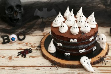 Tatlı Cadılar Bayramı pastası beyaz ahşap masada hayaletler, örümcekler ve kafataslarıyla süslenmiş.