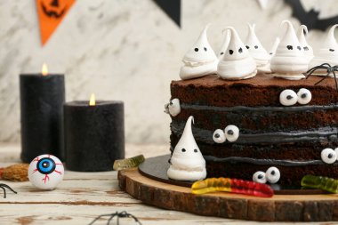 Tatlı Cadılar Bayramı pastası beyaz ahşap masada yanan mumlar, örümcekler, solucanlar ve şekerlerle süslenmiş.