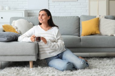 Oturma odasındaki halıya oturmuş, cam bardak sıcak kakaolu güzel bir kadın.
