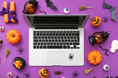 Modern dizüstü bilgisayarlı kompozisyon, farklı dekorasyonlar ve mor arka planda Cadılar Bayramı için mısır şekeri.