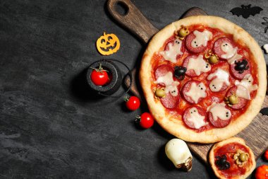 Lezzetli Cadılar Bayramı pizzaları, domatesleri ve koyu arkaplanda süslemeleri olan kompozisyon