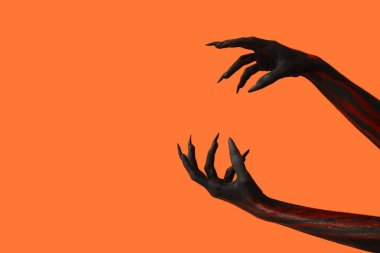 Turuncu arka planda pençeleri olan kara cadı elleri. Cadılar Bayramı