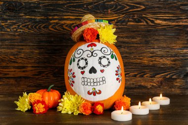 Kafatası boyalı balkabağı, mini sombrero, yanan mumlar ve ahşap arka planda çiçekler. El Dia de Muertos