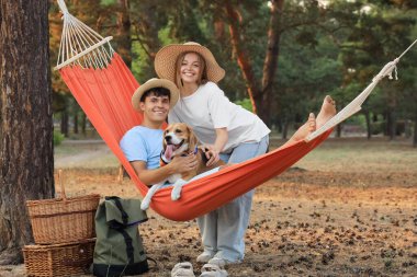 Beagle köpeği ve kız arkadaşıyla dışarıda hamakta dinlenen genç bir adam.