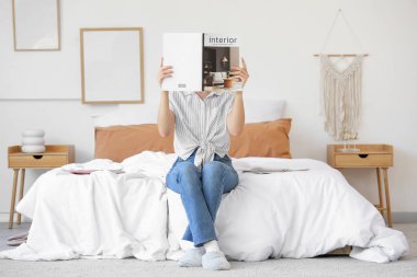 Yatak odasında iç tasarım dergisi okuyan genç bir kadın.