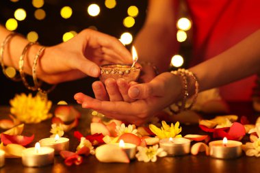 Diwali için güzel bir diya lambası tutan kadınlar. Karanlık arka planda mumlar, çiçekler ve yapraklarla.