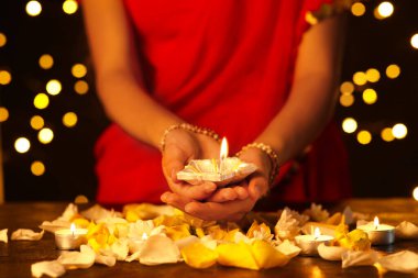 Diwali için güzel bir diya lambası tutan bir kadın. Arka planda mumlar, çiçekler ve yapraklar var.