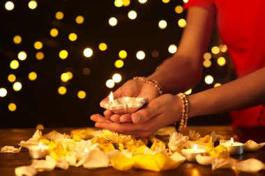 Diwali için güzel bir diya lambası tutan bir kadın. Arka planda mumlar, çiçekler ve yapraklar var.