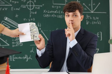 Male teacher showing silence gesture and taking bribe in classroom. Corruption concept clipart