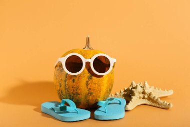 Turuncu arka planda terlikli, güneş gözlüklü ve deniz yıldızlı Cadılar Bayramı kabağı