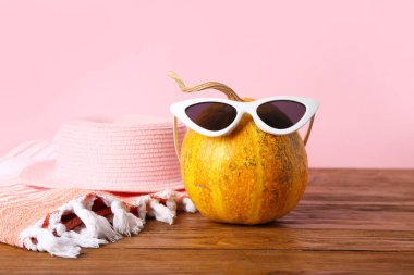 Güneş gözlüklü Cadılar Bayramı kabağı ve pembe arka planda ahşap masa üzerinde şapka