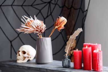 Kurumuş çiçekli vazo ve Cadılar Bayramı için dekore edilmiş şömine rafında yanan mumlar. Yakın plan.