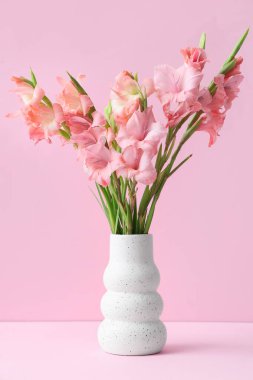 Üzerinde pembe arka planda bir buket güzel gladiolus çiçeği olan vazo.
