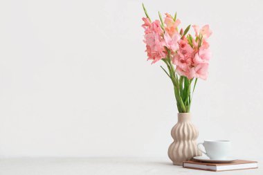 Üzerinde bir buket güzel gladiolus çiçeği, kitap ve kahve olan bir vazo beyaz arka planda.