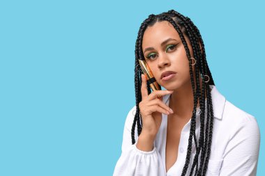 Mavi arka planda maskara tutan güzel makyajlı Afro-Amerikalı genç bir kadın.