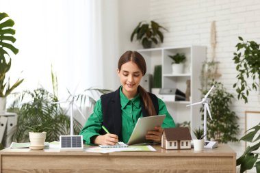 Ofisteki masada tablet bilgisayar ve rüzgar türbini modelleriyle çalışan kadın mühendis.
