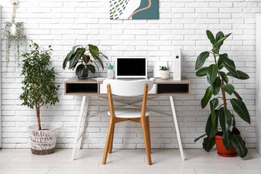 Ofiste beyaz tuğla duvarın yanında boş dizüstü bilgisayarı ve yeşil bitkileri olan işyeri