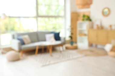 Pencerenin yanında gri kanepe ve kahve masası olan modern oturma odasının bulanık görüntüsü.