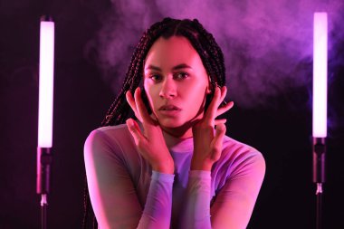 Koyu arkaplanda saç örgüleri ve neon lambaları olan güzel bir Afro-Amerikalı kadın.