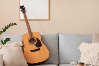 Oturma odasındaki gri koltukta yastıklı gitar.
