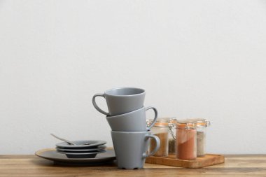 Bardaklar, tabaklar ve baharatlar beyaz duvarın yanındaki ahşap masada.