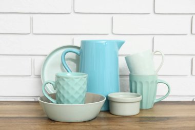 Bardaklar, kaseler ve sürahiler beyaz tuğla duvarın yanındaki ahşap masada.