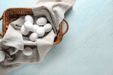 Açık mavi arka planda çiğ tavuk yumurtası ile hasır sepet.