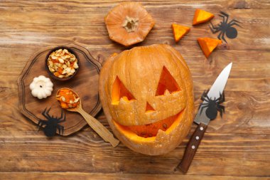 Ahşap arka planda kaşık, bıçak, mum ve dekorla oyulmuş Cadılar Bayramı balkabağı