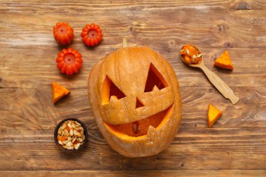 Kaşıkla oyulmuş Cadılar Bayramı kabağı, bir kase tohum ve ahşap arka planda mumlar.